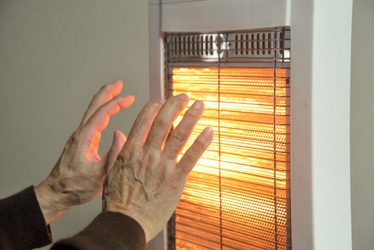 Senior hands warming themselves by an electric heater